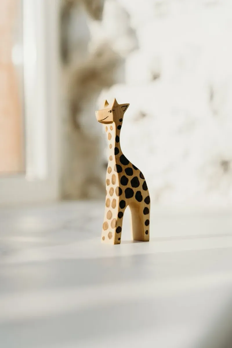 A handcrafted wooden giraffe toy on a marble surface in warm natural light