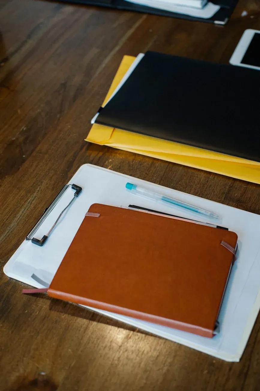 A leather planner, clipboard and document folders on a wooden desk, viewed from above