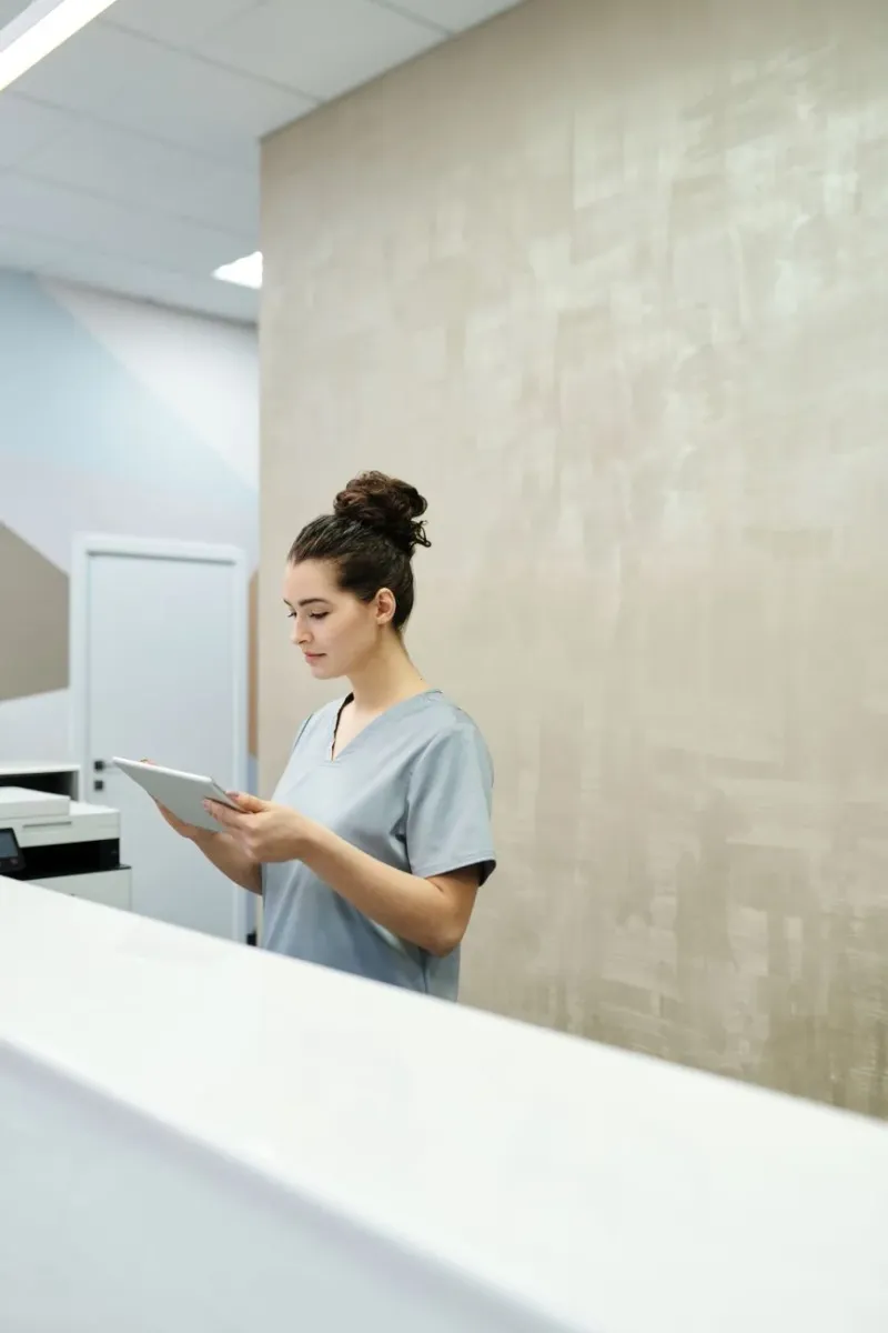 An allied health professional in scrubs reviewing a tablet by a window