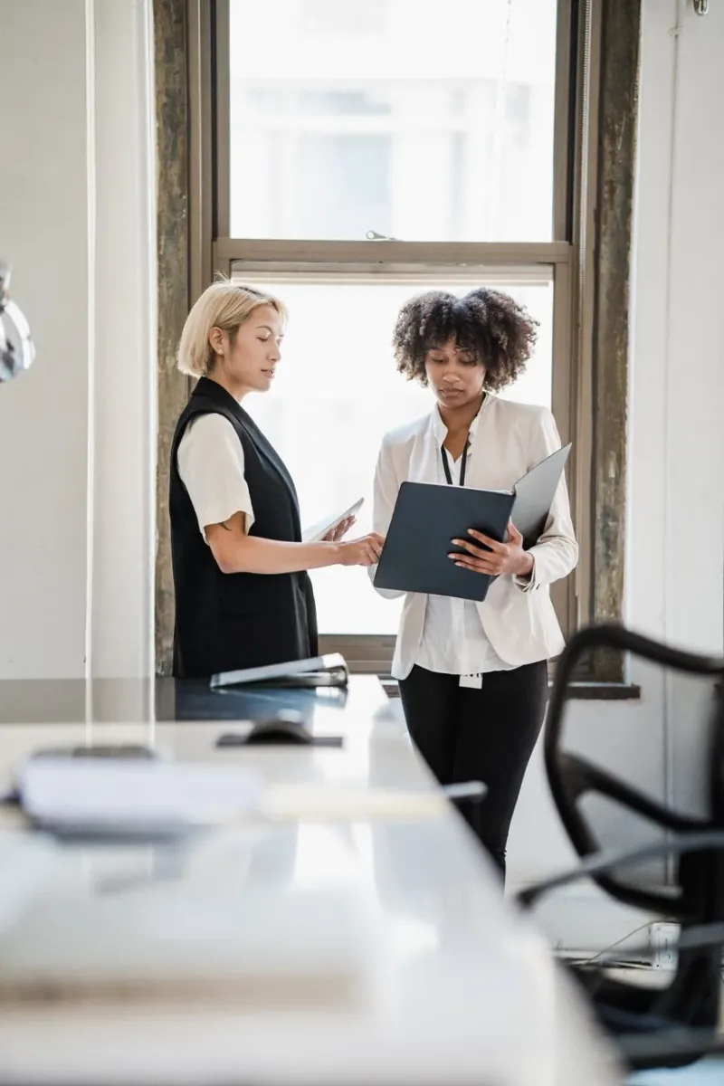 Two professionals reviewing a folder together in soft window light