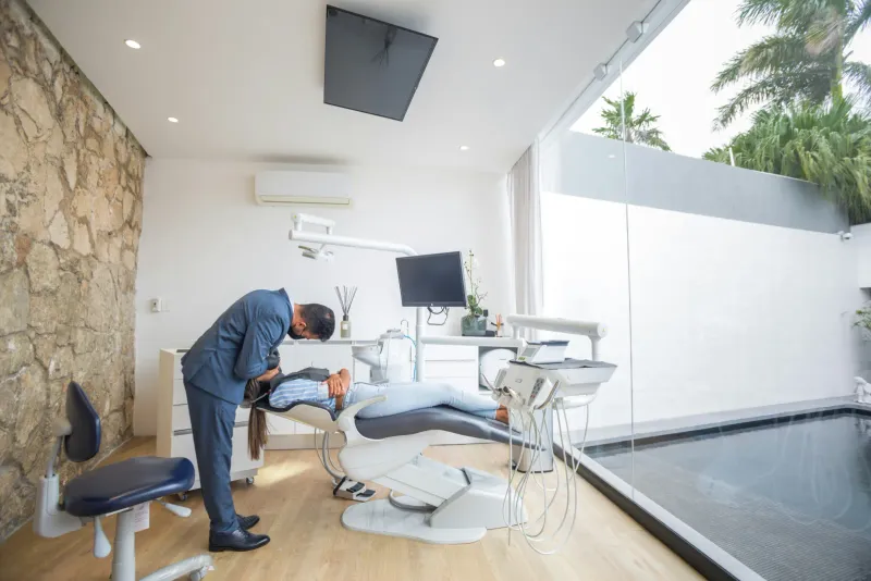 A dentist treating a patient in a bright modern dental clinic with a natural stone feature wall and daylight