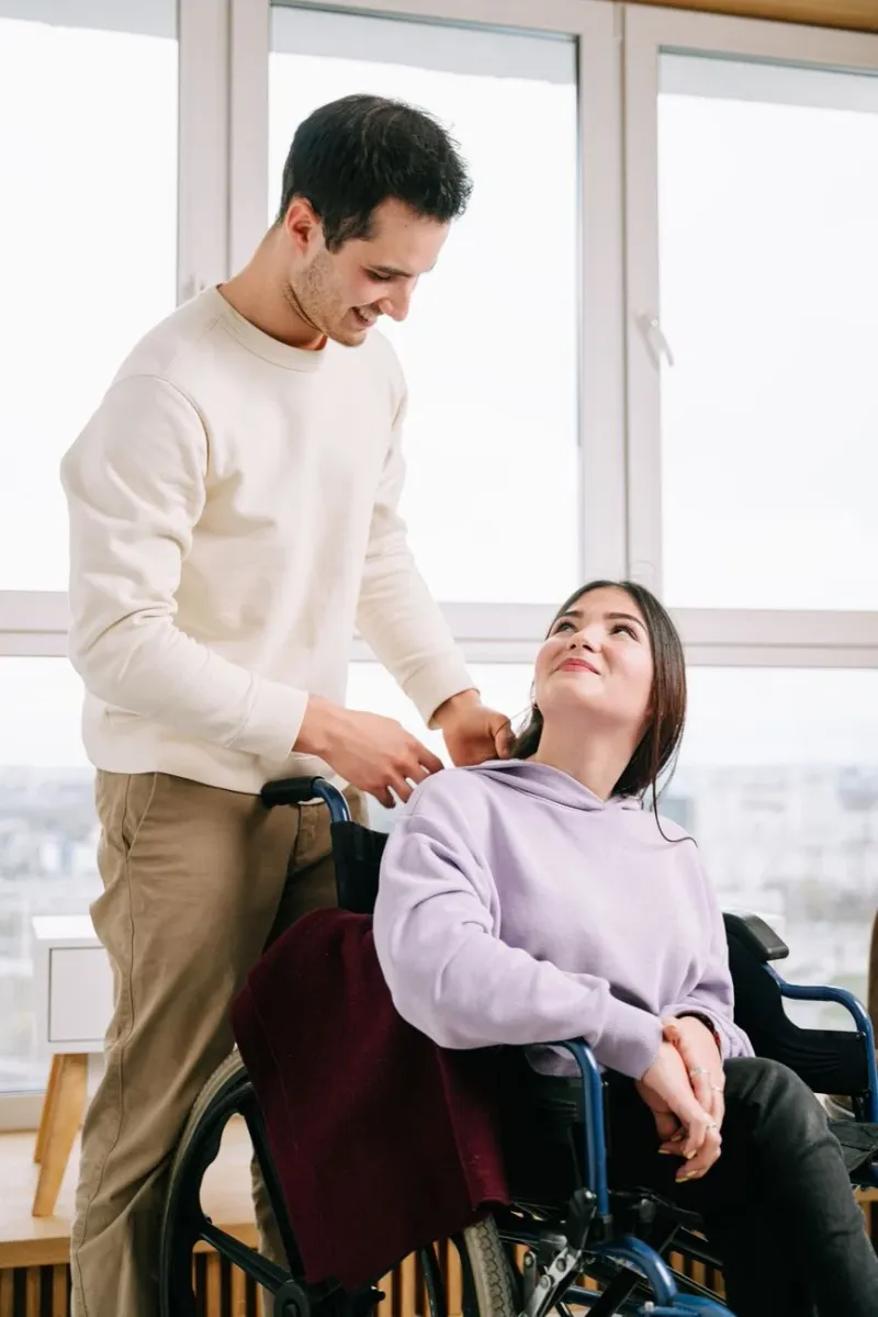 A support worker assisting a smiling woman in a wheelchair by a window