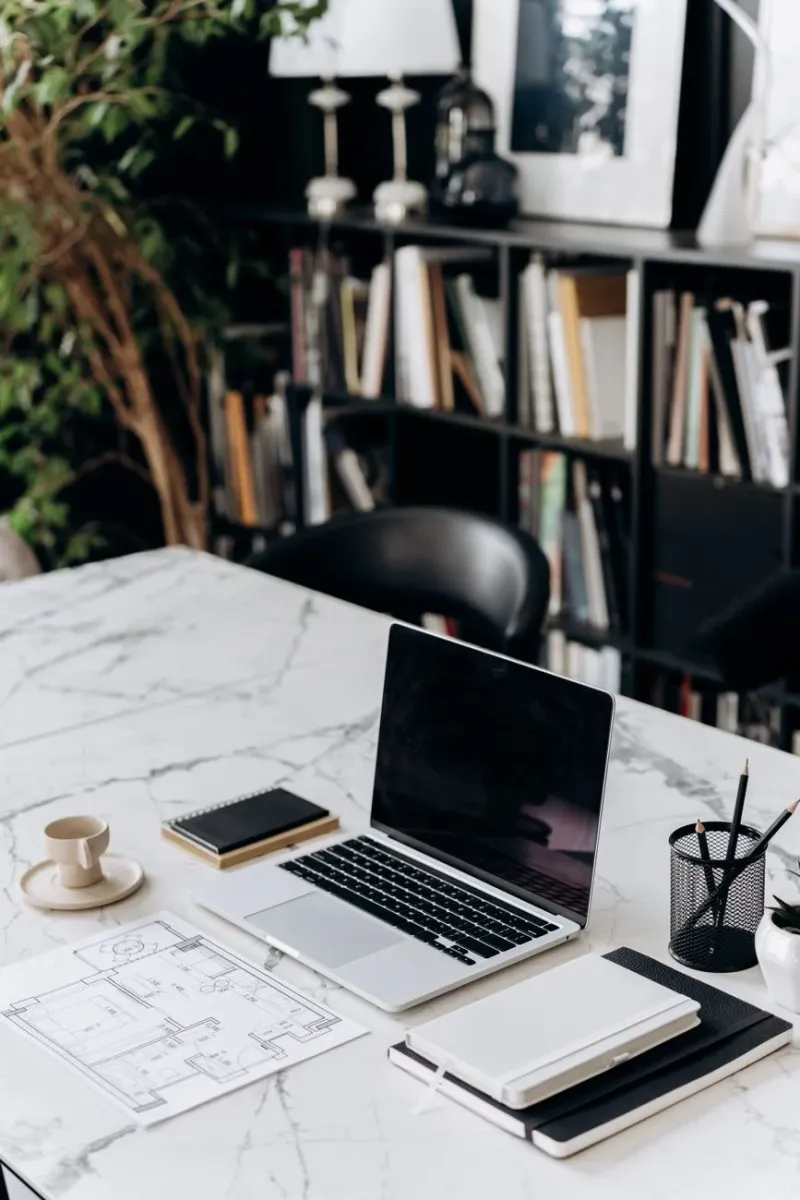 A marble desk workspace with a laptop, notebook and coffee in natural light