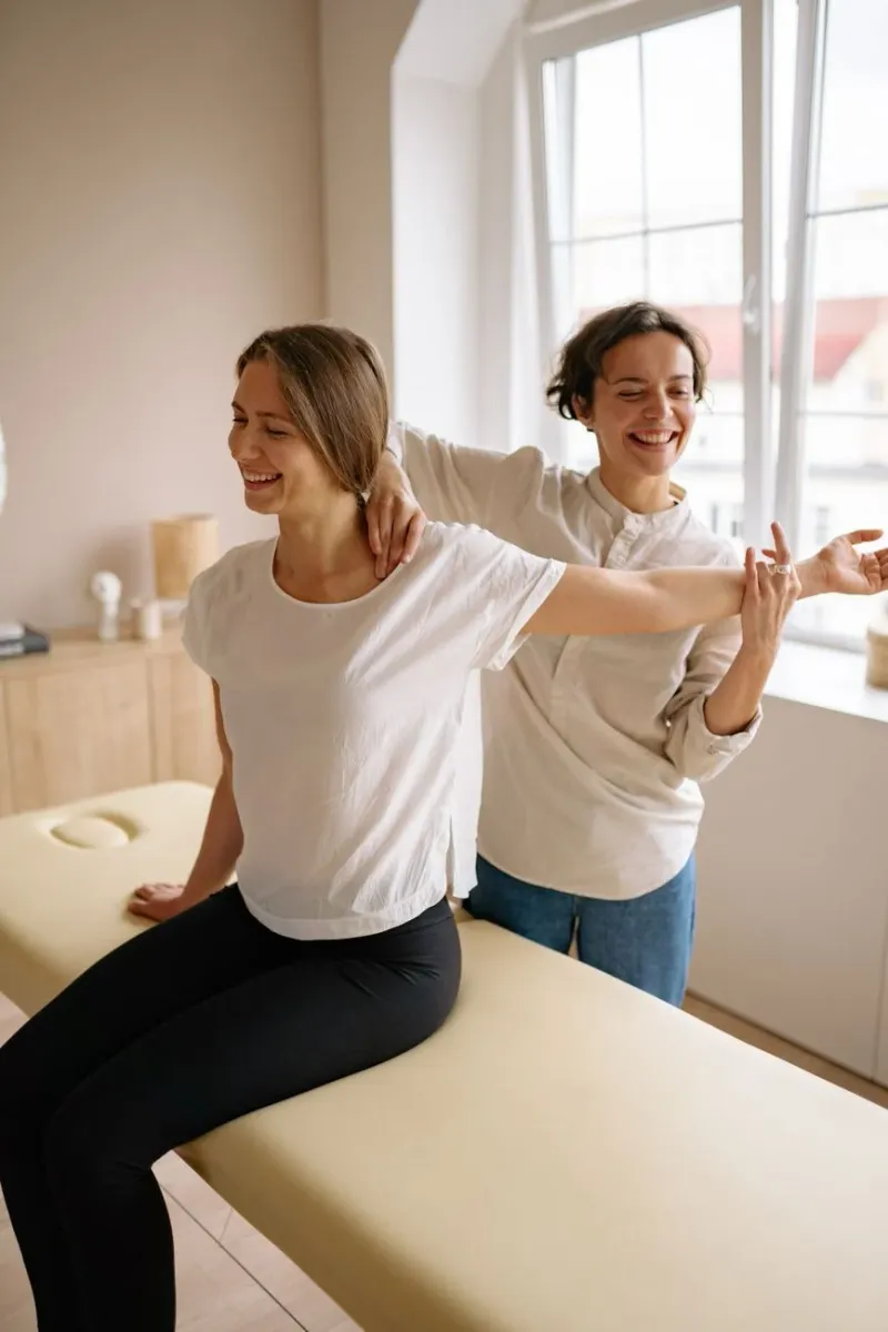 Two people performing stretching exercises by a bright window